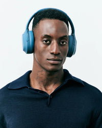 A person with dark skin tone and short black hair is wearing the Oasis Core Active Noise Cancelling Headphones.