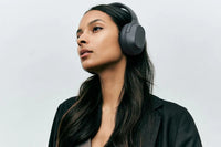 A person with medium skin tone and long dark brown hair is wearing the Cave Core Noise Cancelling Headphones.