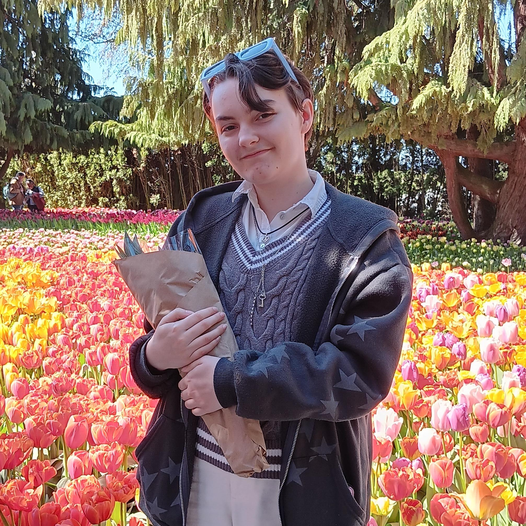 Young person standing in a tulip field holding tulips