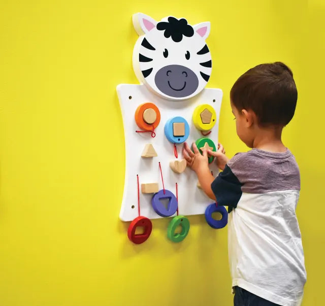 A child with light skin tone and short brown hair pushes the star shape onto the Zebra Activity Wall Panel.