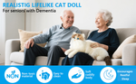 Two seniors sit on a couch and smile while one of them holds the Therapy Cat Plush.
