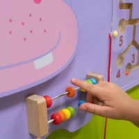 A small hand with light skin tone hovers over the rainbow abacus on the Hippo Activity Wall Panel.