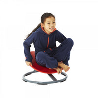 A child with medium light skin tone and long bown hair that is pulled back into a ponytail is sitting crossed legged on the Gonge Carousel. Their knees are pointed up and they are holding onto the seat.