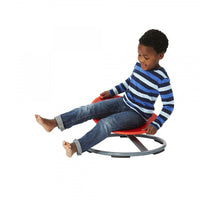 A child with dark skin tone and short black hair is sitting on the Gonge Carousel. Their legs are splayed out in front of them and they are holding onto the seat.