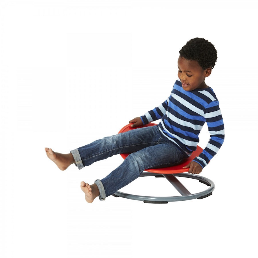 A child with dark skin tone and short black hair is sitting on the Gonge Carousel. Their legs are splayed out in front of them and they are holding onto the seat.