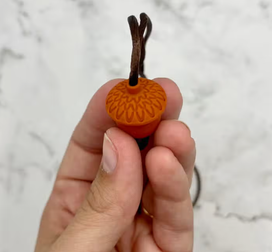 A hand showing the design on the top of the Acorn Fidget Chewable Jewelry Necklace.