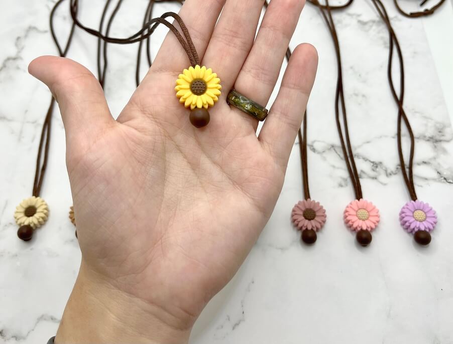 A hand holds up a yellow Small Flower Silicone Chewy Fidget Necklace.