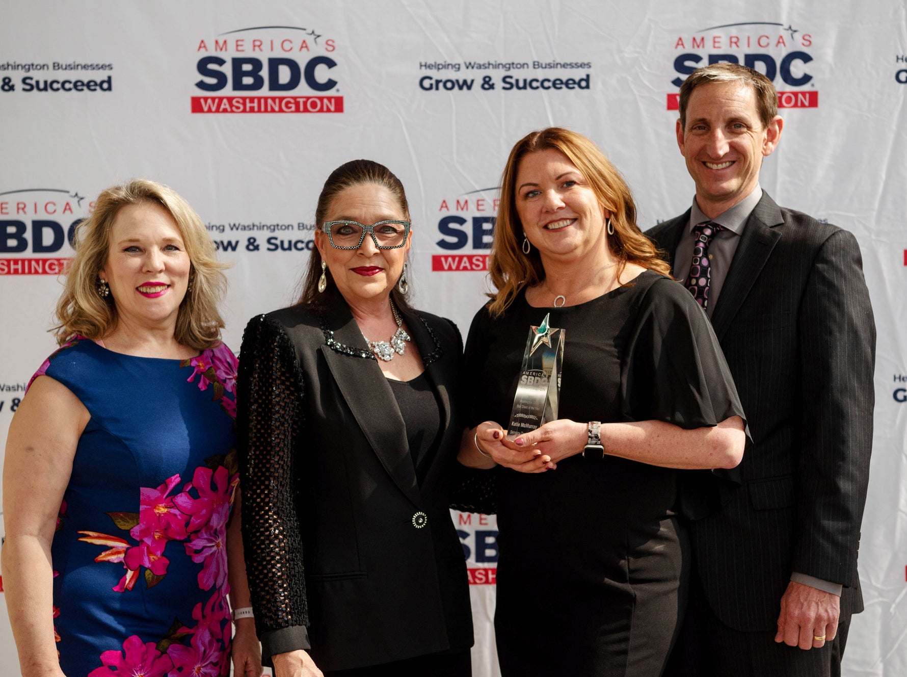 four people smiling at the camera with an award