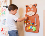 A child with light skin tone and short brown hair moves the wooden beads on the Horse Activity Wall Panel.