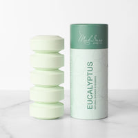 A stack of five green Eucalyptus Mad Sass Soap Co Shower Steamers stands next to the green product package.