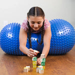 A child lays in the middle of the Peanut Stability Ball on her belly while playing with blocks.