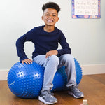 A child sits in the middle of the Peanut Stability Ball and smiles at the camera.