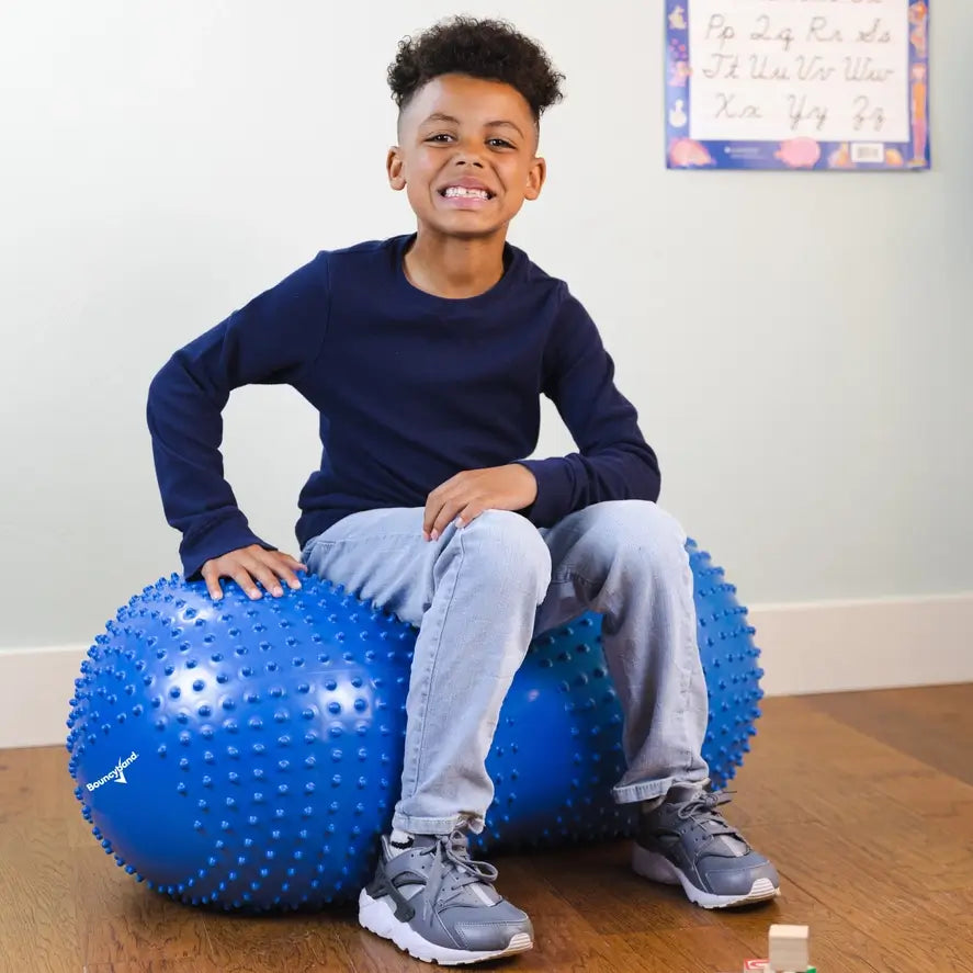 A child sits in the middle of the Peanut Stability Ball and smiles at the camera.