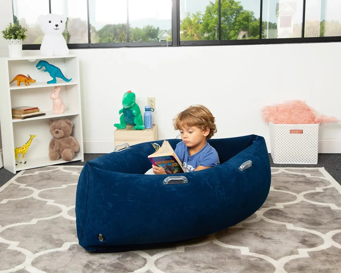 A small child opens a book while relaxing in the blue 48" Peapod.