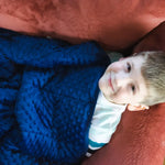 A child looks up while laying on the couch, under the covers with the Bouncyband Kids Soft Fleece Sensory Weighted Blanket - 7 lb.
