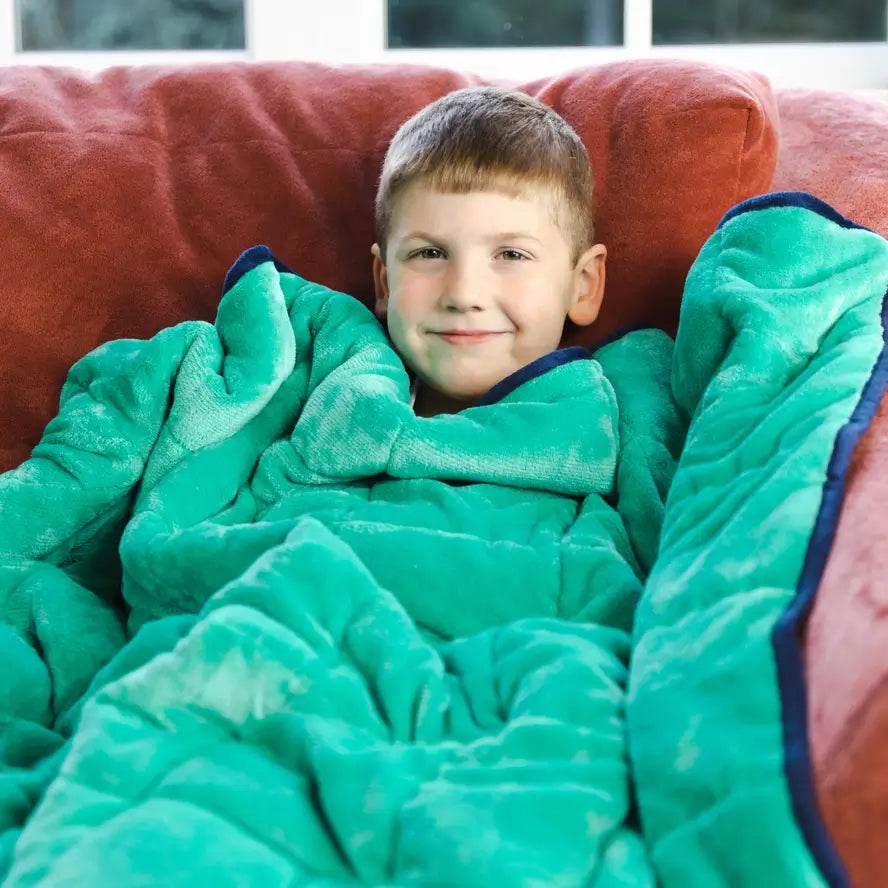 A child cuddles under the Bouncyband Kids Soft Fleece Sensory Weighted Blanket - 7 lb with the smooth plush texture facing out.