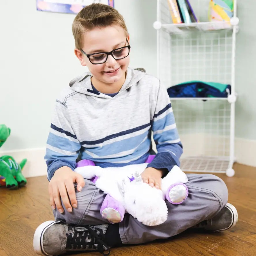 A child looks down at the Weighted Washable Lap Pad Unicorn in their lap.