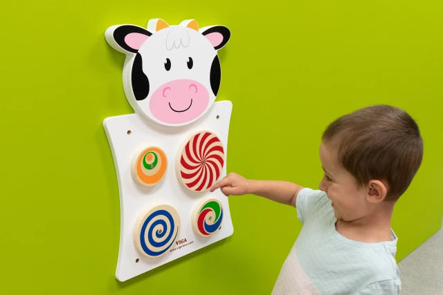 A child with light skin tone and short brown hair pushes one of the wheels on the Cow Activity Wall Panel. 
