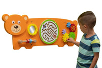 A child with light skin tone and short brown hair plays with the colorful cogs on the Bear Activity Wall Panel.