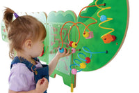 A child with light skin tone and a blonde top pony tail plays with some wooden beads on the Crocodile Activity Wall Panels.