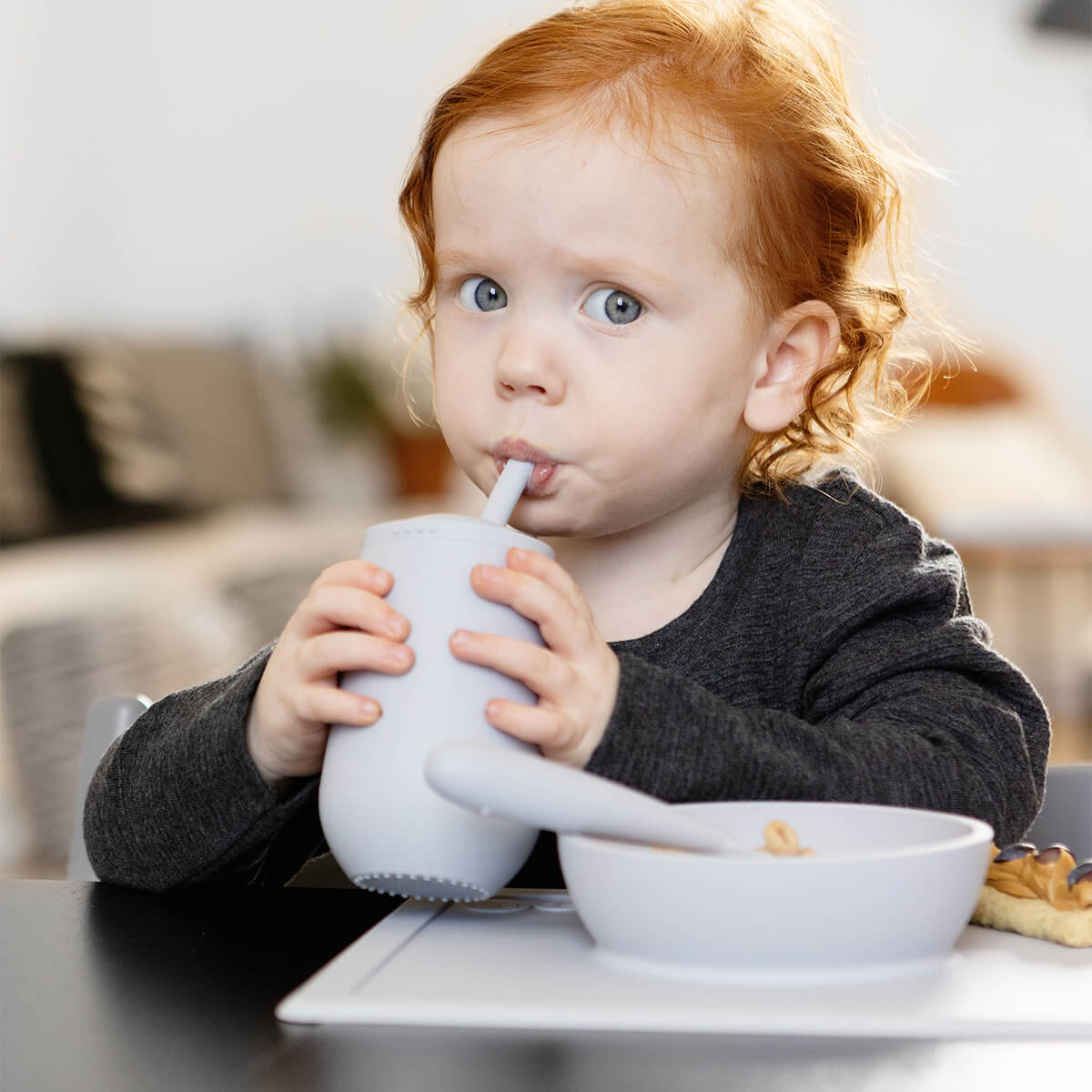 A child looks suspicious while drinking from the EZPZ Pewter Cup + Straw System.