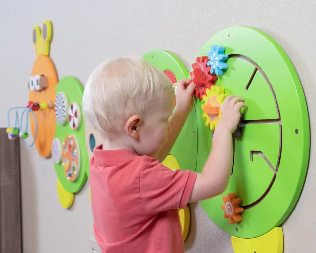 A child with light skin tone and blonde hair plays with the cog maze on the Caterpillar Activity Wall Panels.