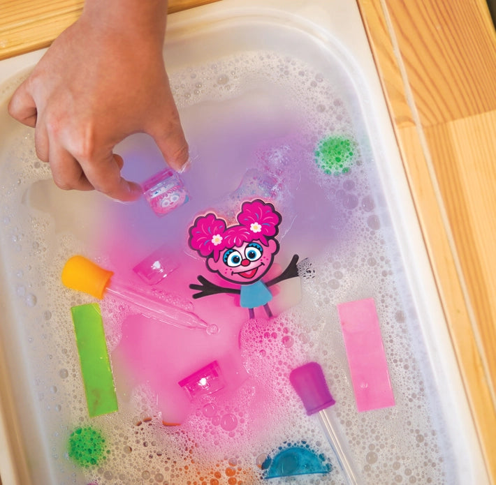 The Abby Cadabby Sesame Street Glo Pal floats in a soapy tub with other light up cubes and droppers.