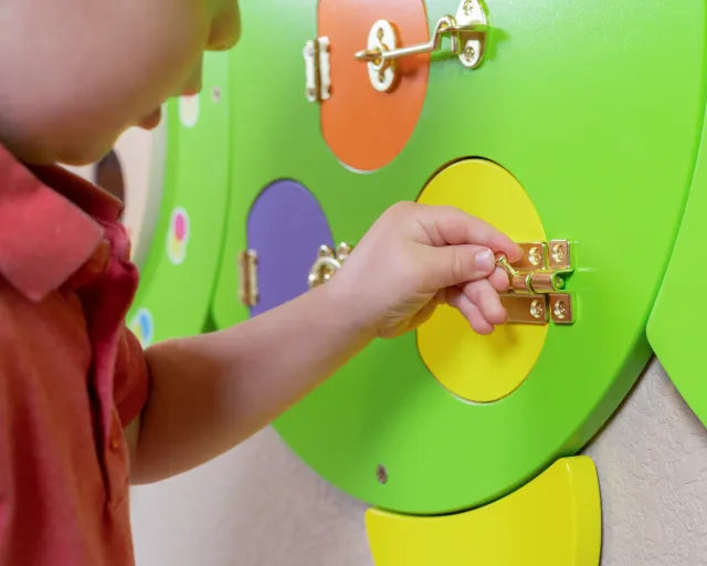 A child with light skin tone plays with the locks on the Caterpillar Activity Wall Panels.
