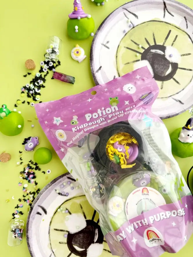 A package of the Potion KidDough Play Kit is laying on two green eye shaped plates. 