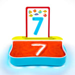 A number 7 is displayed on a card above a light-up table with orange sand in which someone has written a 7.