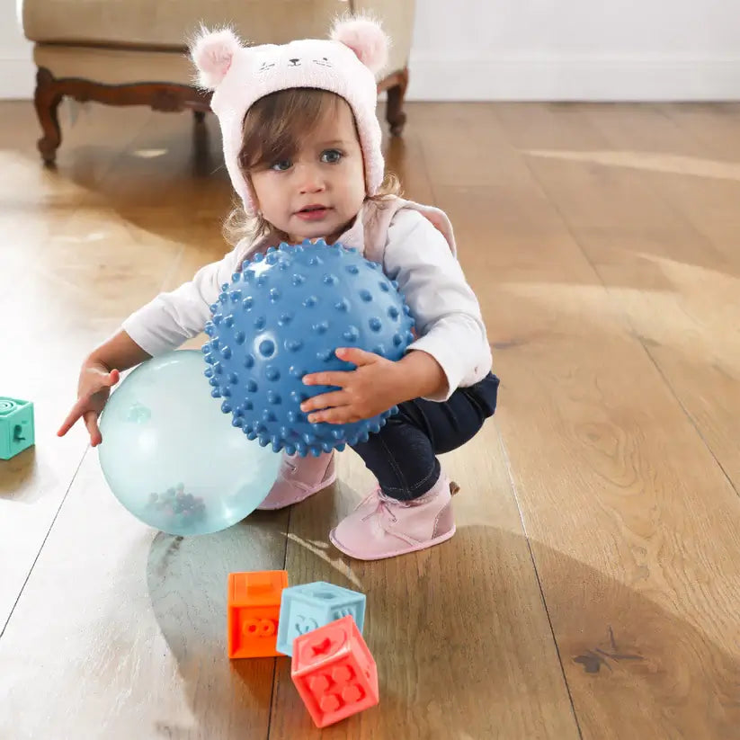 A child squats and holds the Rainbow Soft Ball and a spiky blue ball.