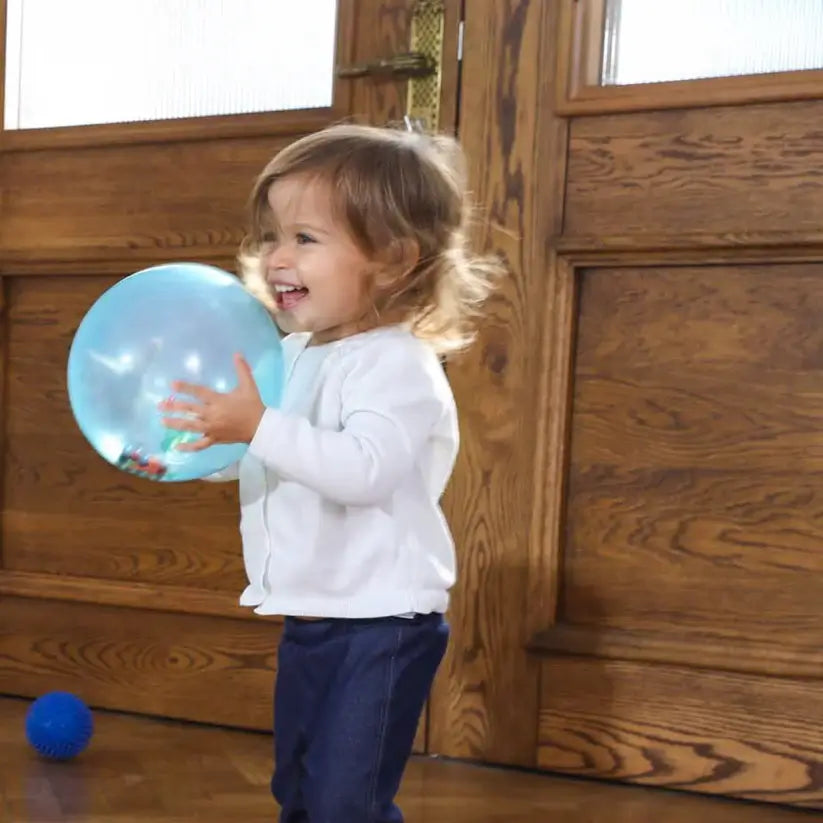 A child laughs and holds the Rainbow Soft Ball close to her chest.