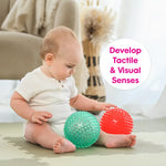 A baby lightly touches the spiky Scented Sensory Balls on the floor in front of him.