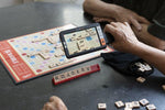 A hand holds up the explore 5 Pocket Size Video Magnifier to a game of Scrabble.