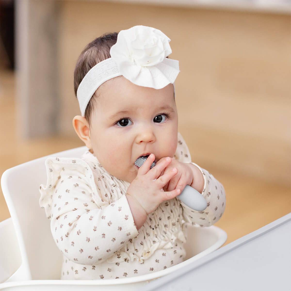 A baby puts the Pewter ezpz Baby-Led Toothbrush in its mouth.