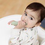 A baby puts the Sage Baby-Led Toothbrush in its mouth.