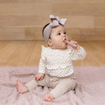 A toddler sits up and puts the Blush ezpz Baby-Led Toothbrush in its mouth.