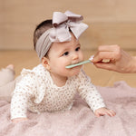 A baby on its belly closes its mouth around a Sage Tongue Depressor by ezpz.