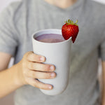 A child holds the cup portion of the Pewter 14 oz Cup + lid with a purple smoothie in it.