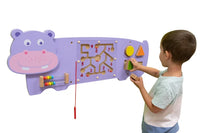 A child with light skin tone and short brown hair plays with the shapes on the Hippo Activity Wall Panel.