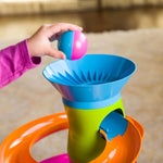A young child's hand drops a bi-colored ball into the top of the RollAgain Tower.