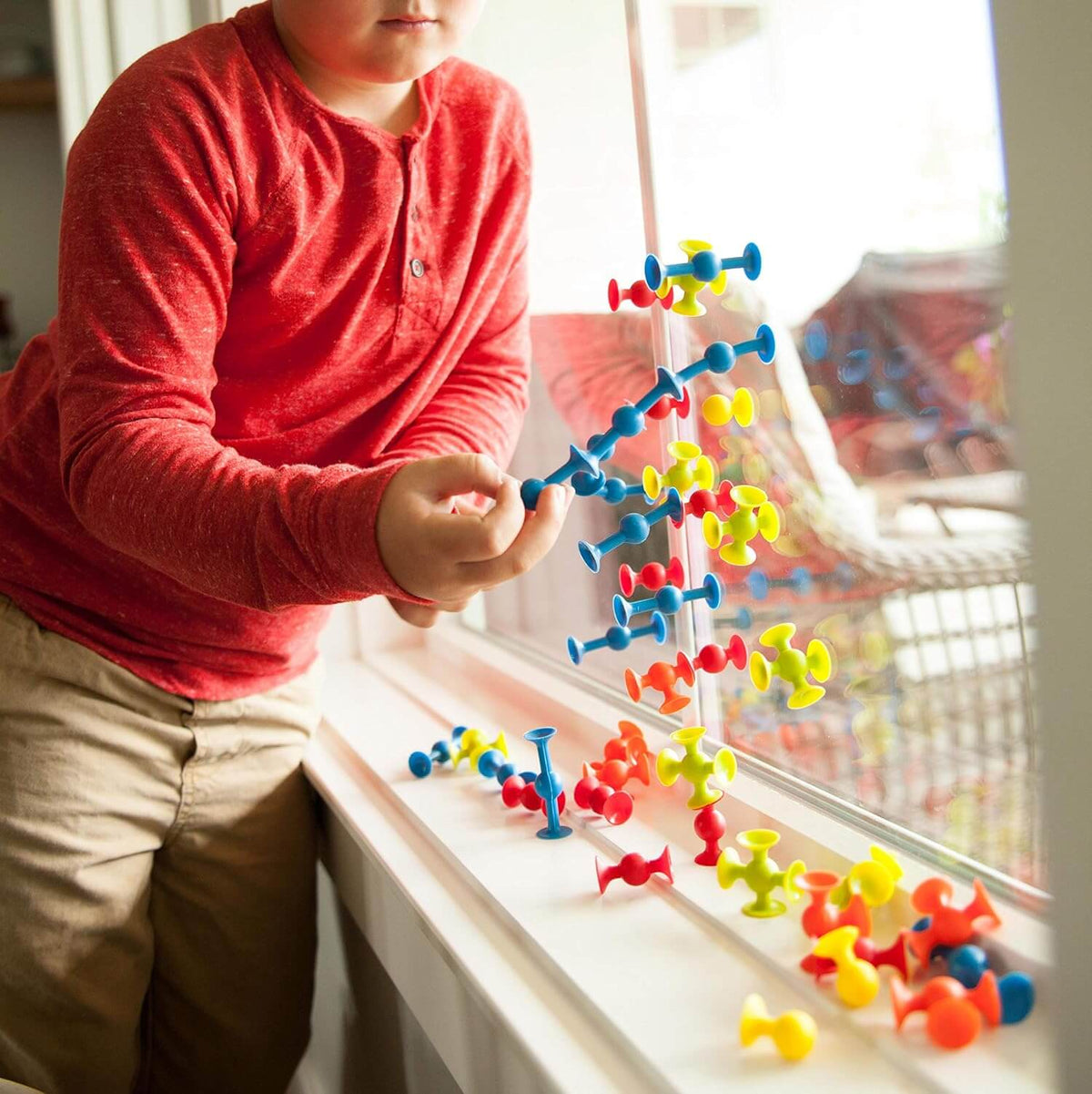 A child links Mini Squigz together that are adhered to a window.