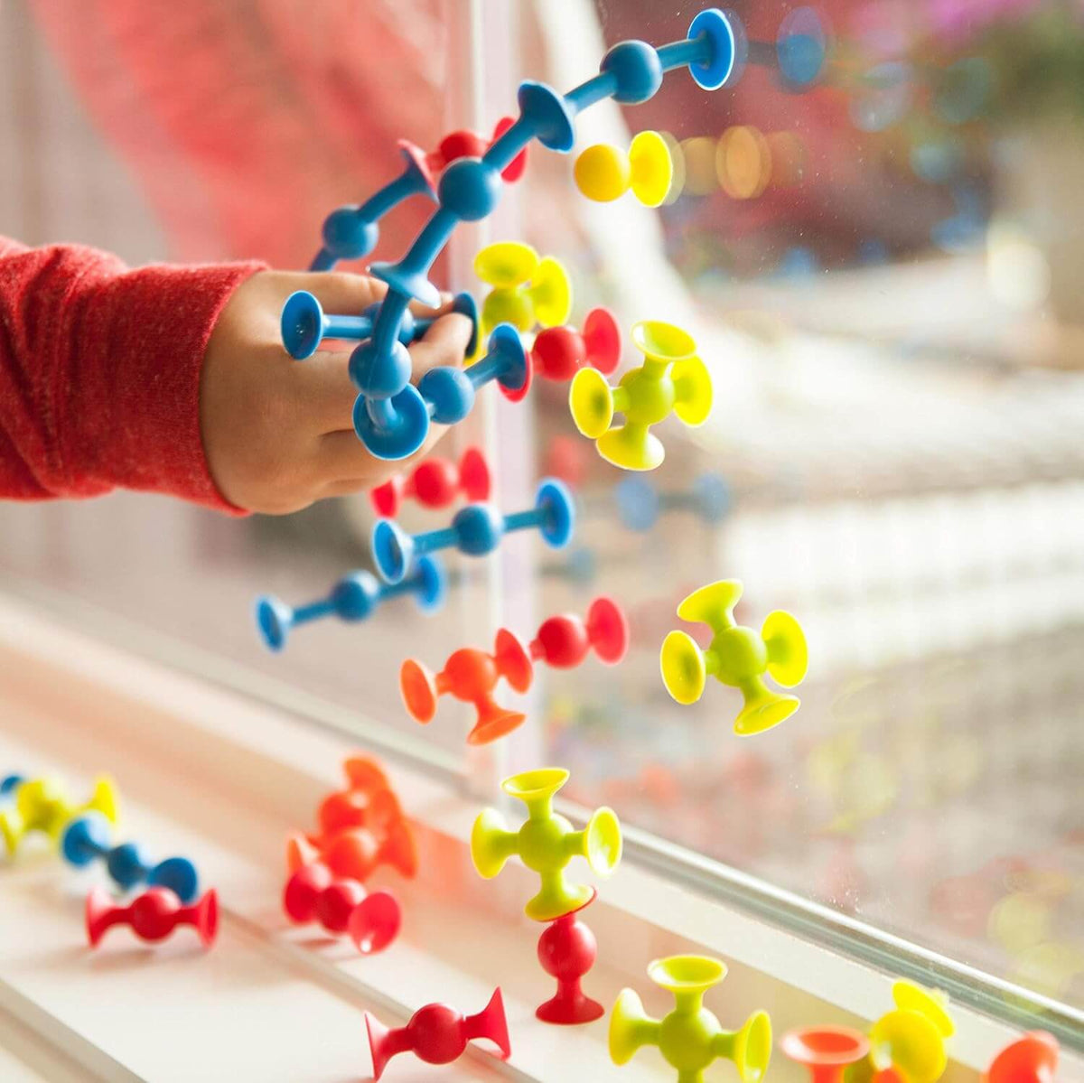 A child hand presses the blue Mini Squigz to a window surface.