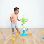 A child laughs while standing in the midst of a flood of multicolored balls falling from the SpillAgain tower.
