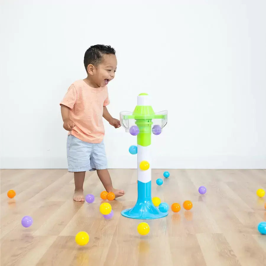 A child laughs while standing in the midst of a flood of multicolored balls falling from the SpillAgain tower.