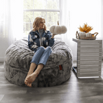 A woman sits on the Faux Chinchilla Bean Bag Convertible Bed as a chair and holds up a white decorative pumpkin.