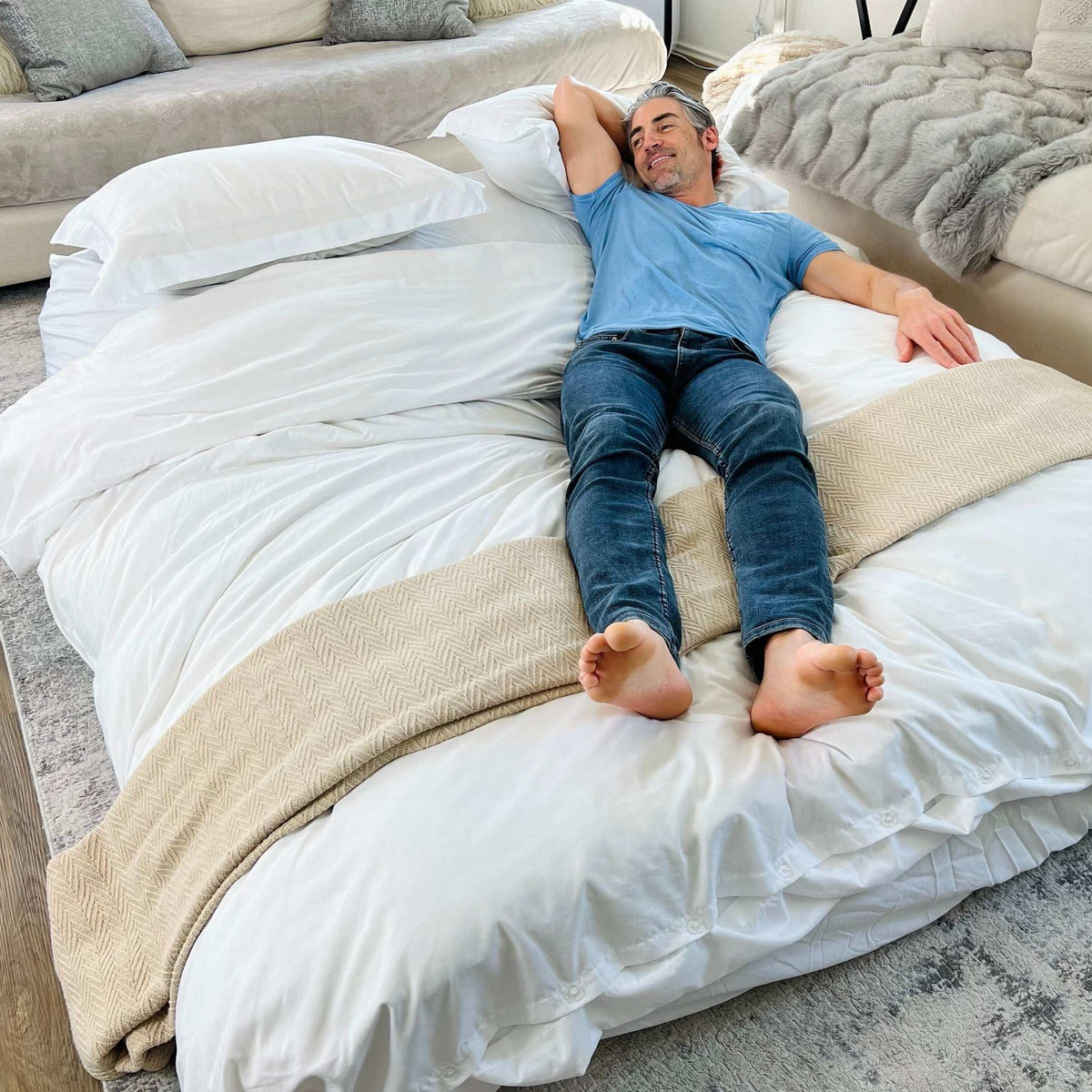 A man lays across the unfolded bed made up for sleeping.