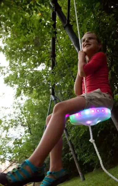 A child sits on the lit-up Flying Saucer LED Swing.
