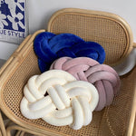 Three Fried Dough Twist Plush Sensory Pillows on a wicker chair.