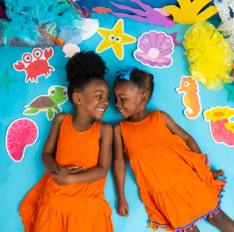 Two children lay down on a sea foam blue surface, surrounded by the Guppy Grips.